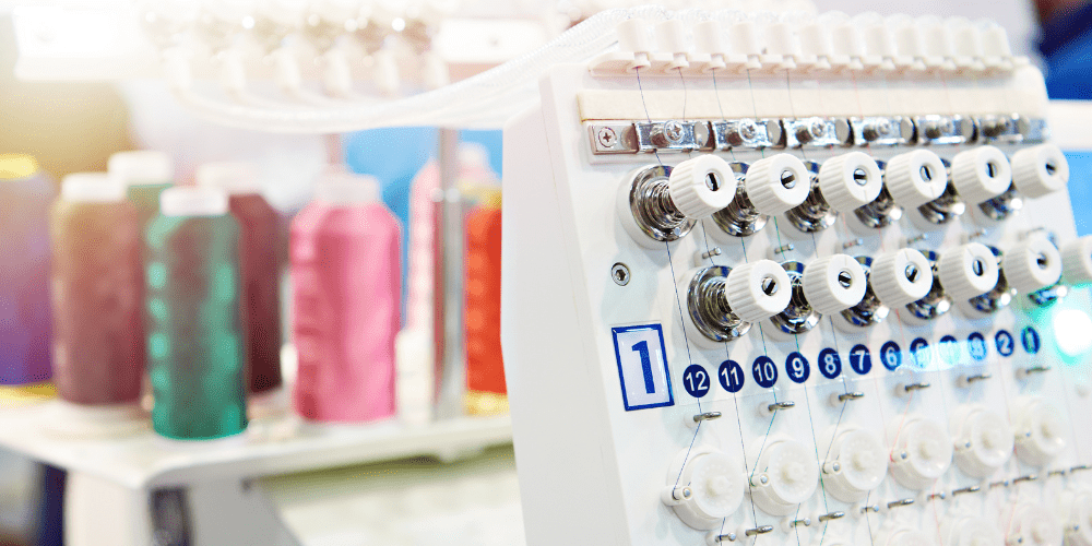 Close-up of a multi-needle embroidery machine with threaded spools and tension dials, ready for high-volume custom embroidery production using colorful threads.