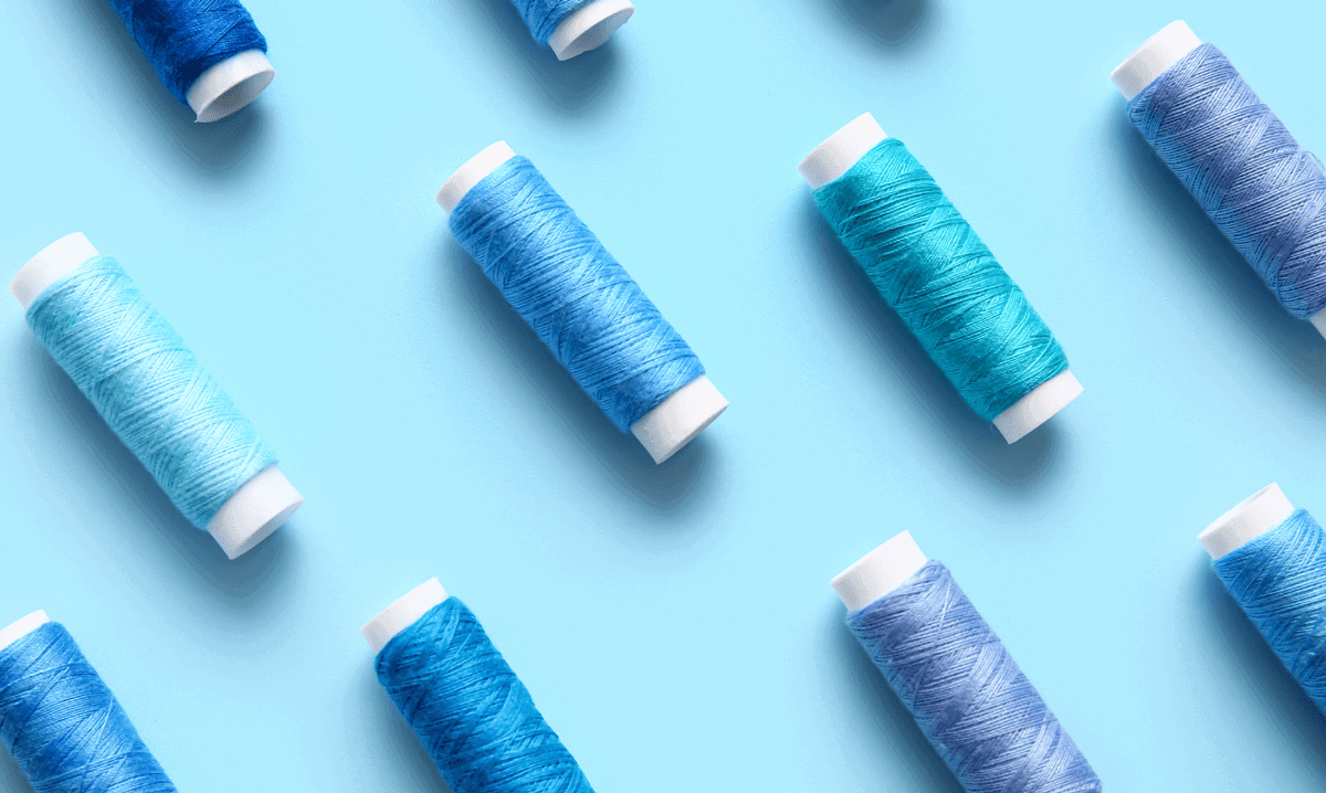Vibrant blue spools of thread on a light blue background, ideal for embroidery and sewing projects.